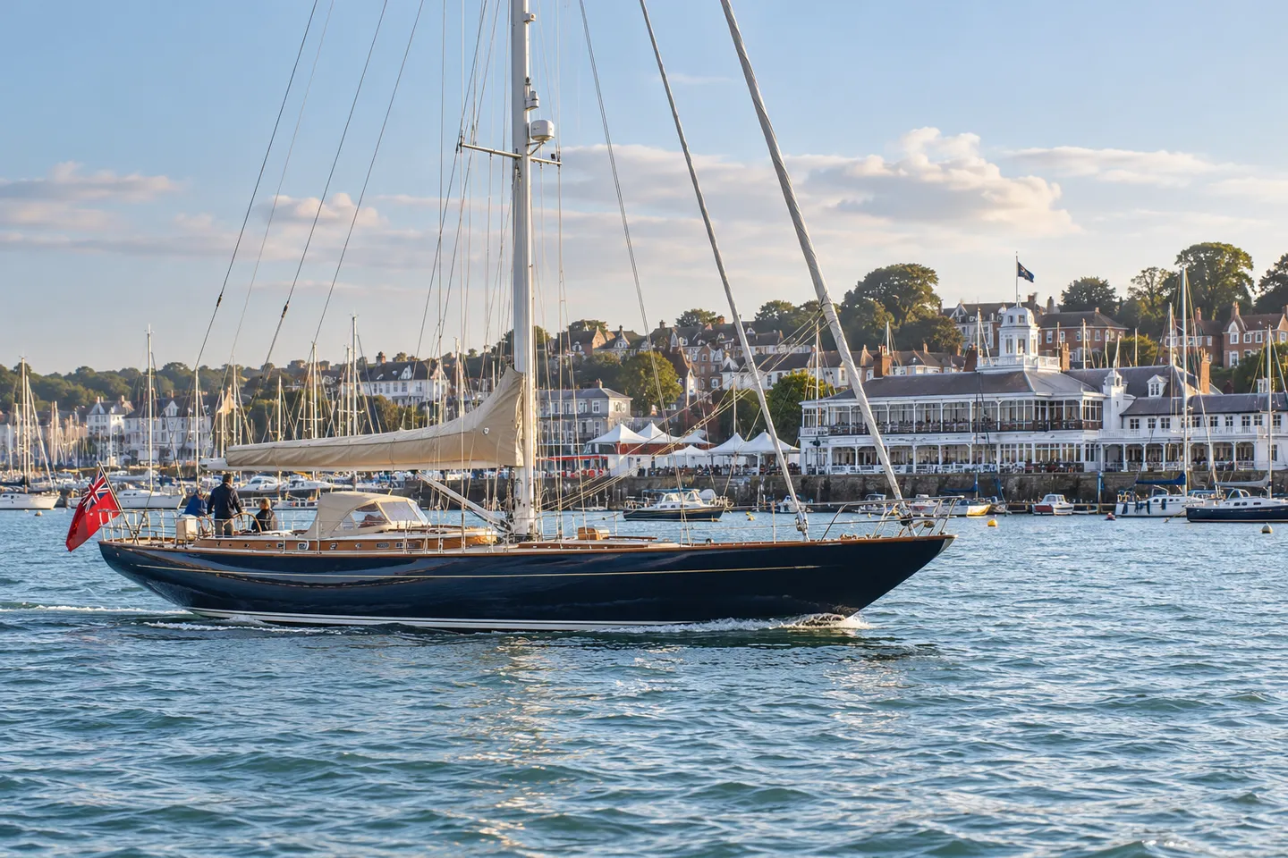 A classic navy-hulled sailing yacht passing the Cowes waterfront